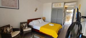 een slaapkamer met een bed met een gele deken en 2 stoelen bij "Studio Bellevue" Terrasse et Deck vue mer-Accès piscine in Le Diamant