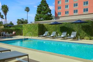 a swimming pool with chairs and umbrellas next to a building at Courtyard by Marriott Los Angeles Westside in Los Angeles