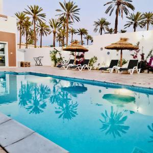 una piscina con sillas, sombrillas y palmeras en Dar selim en Midoun
