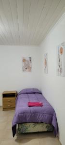 Un dormitorio con una cama morada en una habitación blanca en casa la infancia en Perito Moreno