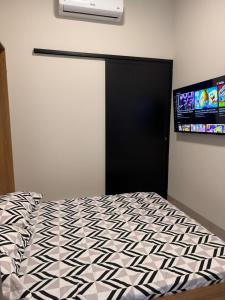 1 dormitorio con 1 cama y TV en la pared en Studios Soho Bongiovani, en Presidente Prudente