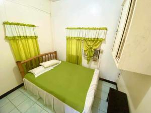a small bedroom with a green bed and yellow curtains at Tamari's Rest house (Small house) in Lian