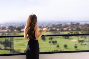Una donna che tiene un bicchiere di vino davanti a una finestra di VEA Newport Beach, a Marriott Resort & Spa a Newport Beach