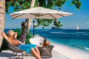 a man laying in a chair under an umbrella on a beach at The Villa Gita Segara in Candidasa