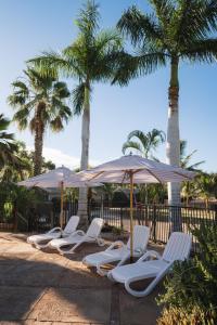 a row of lounge chairs and umbrellas on a beach at Ningaloo Caravan and Holiday Resort in Exmouth