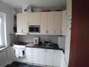 cocina con armarios blancos, fregadero y microondas en Naza cool villa! en Malmö