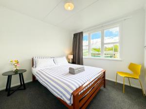 a bedroom with a bed and a window and a yellow chair at Serene Home in Whangarei in Whangarei