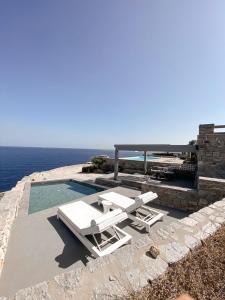 a pool with two white lounge chairs and the ocean at Cave Suite in Sarakíniko