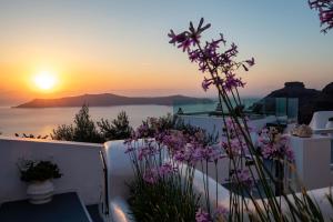 Santorini View Studios - Firostefani Caldera في فِروستيفاني: إطلالة على غروب الشمس من شرفة مع زهور أرجوانية