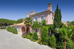 ein großes rosafarbenes Haus mit Bäumen und Sträuchern in der Unterkunft Quinta Jacintina - My Secret Garden Hotel in Vale do Lobo