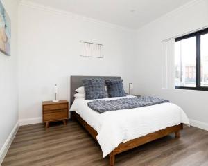 a white bedroom with a large bed with blue pillows at Modern Home in the Heart of Bankstown in Bankstown