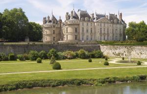 a large castle with a grassy yard and a river at Spacieuse maison de village in Luché-Pringé