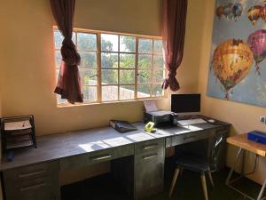 ein Büro mit einem Schreibtisch mit einem Computer und einem Fenster in der Unterkunft Charming Cottage in the wilderness on 5 Acres in Lusaka