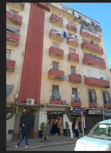 Un grand bâtiment avec des gens qui marchent devant lui dans l'établissement Farah, à El Madania