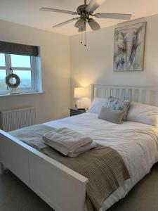 a bedroom with a white bed with a ceiling fan at Spacious Stylish House Close to M4 Private Parking in Magor
