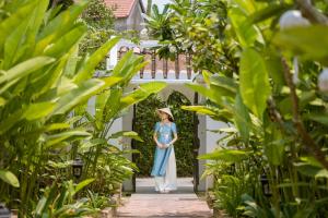 a woman in a blue dress walking through a garden at Nghe Garden Resort Hoian in Hoi An