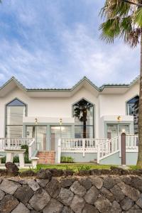 a white house with a palm tree at Le Village Aewol G in Jeju