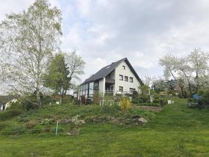 ein weißes Haus auf einem Grashügel in der Unterkunft Ferienwohnungen Thomsen Bergdorf Pobershau in Marienberg