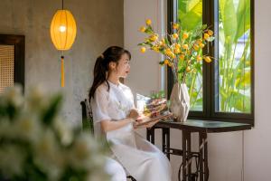uma mulher de vestido branco sentada à mesa com um bolo em Nghé Garden Resort Hội An by Label6 em Hoi An