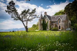 une ancienne maison en pierre dans un champ de fleurs dans l'établissement Ardrhu House Fort William - Serviced Luxury Scots Baronial Country House, à Fort William