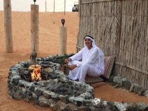 un hombre sentado frente a un pozo de fuego en Margham Desert Safari Camp, en Margham