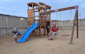 dwójka dzieci bawiących się na placu zabaw w piasku w obiekcie Margham Desert Safari Camp w mieście Margham