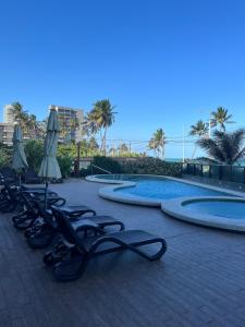 a pool with chaise lounges and umbrellas in front at Suíte 511, do Hotel Ritz Suítes in Maceió