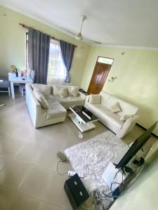 Sala de estar con 2 sofás blancos y TV en A private self contained room in a home away from home en Dar es Salaam