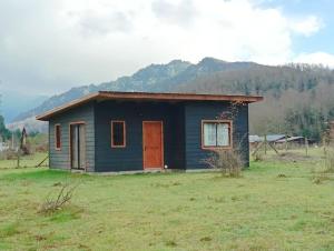 a small blue house with a red door in a field at Cabaña Kallfü Mahuida in Panguipulli