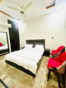 een slaapkamer met een wit bed en 2 rode stoelen bij Hotel Highway Link in Karachi