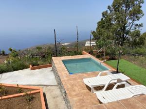 una piscina con 2 sillas blancas y una piscina en helios casa vacacional, en Puntagorda