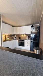uma cozinha com armários brancos e um frigorífico preto em Cosy cabin in North-Norway, Nearby Senja. em Sorreisa