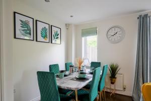a dining room table with green chairs and a clock at Cherish Stays spacious & amazing 3 Bed House in Hayes & Heathrow in West Drayton