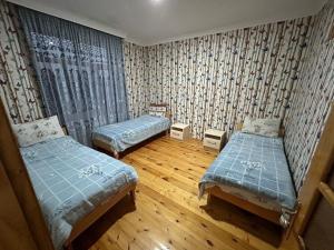 Habitación con 2 camas, cortinas y suelo de madera. en SeMa Qonaq Evi, en Zaqatala