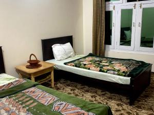 a bedroom with two beds and a table and a window at Moon Light Guest House Khaplu in Khaplu