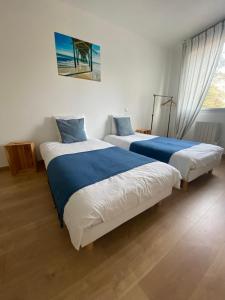 two beds with blue and white sheets in a bedroom at Bel appartement à 200m de la plage in Barneville-Carteret