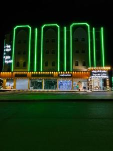 un gran edificio con luces verdes delante de él en Bahget Eljouf Furnished Apartment, en Aţ Ţuwayr