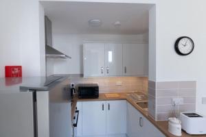 a kitchen with white cabinets and a clock on the wall at Helensburgh Holiday Apartment in Helensburgh