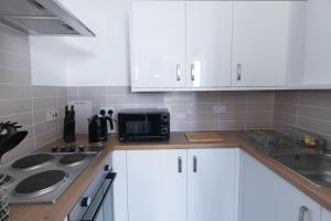 uma cozinha com armários brancos e um micro-ondas preto em Helensburgh Holiday Apartment em Helensburgh