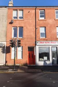 um edifício de tijolos com uma porta vermelha numa rua em Helensburgh Holiday Apartment em Helensburgh