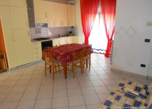 a kitchen with a table and chairs and a kitchen with red curtains at Ferienwohnung für 4 Personen 2 Kinder ca 60 qm in Rosolina Mare, Adriaküste Italien Venedig und Umgebung in Rosolina