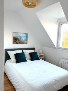 um quarto com uma cama branca e almofadas azuis em Charmante maison familiale em Ouistreham