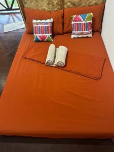 an orange bed with two towels and pillows on it at HIRAYA Camp Site - FREE use of SCOOTER for NIPA HUTS in El Nido