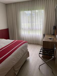 a bedroom with a bed and a desk and a window at Flat Incrível - Livyd Angra dos Reis - Hotel do Bosque 3p in Angra dos Reis