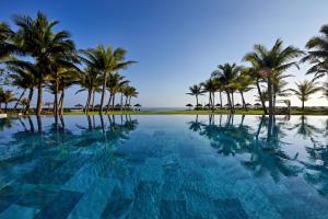 a pool with palm trees and the ocean at Wyndham Hoi An Royal Beachfront Resort & Villas in Hoi An