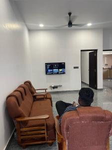 MATHER RAJAGIRI FURNISHED APARTMENTS في Alwaye: رجل يجلس على أريكة لمشاهدة التلفزيون في غرفة