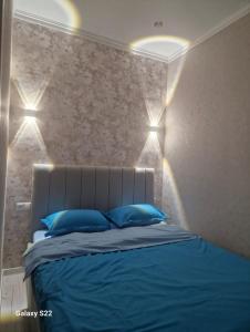 a bedroom with a bed with blue pillows and lights at Квартира Достар in Karagandy