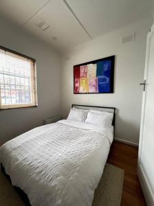a bedroom with a white bed with a painting on the wall at Princes Cottage In Prahran, On Chapel St in Melbourne