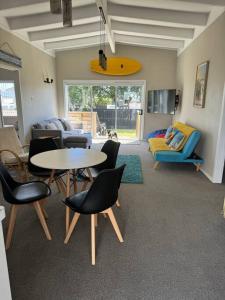 ein Wohnzimmer mit einem Tisch, Stühlen und einem Surfbrett in der Unterkunft Ultimate Family Holiday - Pet Friendly! in Papamoa