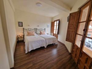 1 dormitorio con 1 cama con sábanas blancas y suelo de madera en Los Cuatro Caños, en Madrigal de la Vera